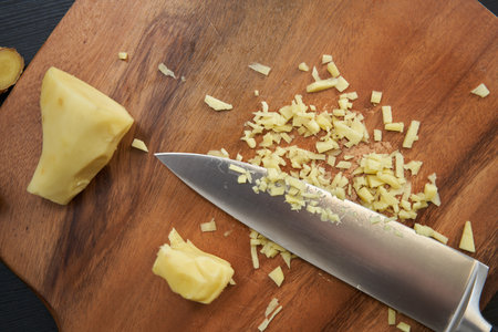 Man chef chopping ginger finely on a wooden board with a very sharp knife