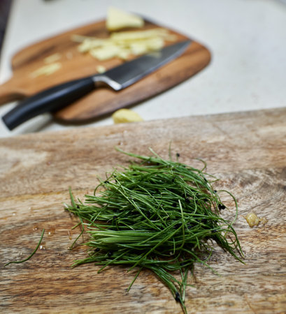 Chives sprouts on a wooden board with chopped ginger in backgroundの写真素材