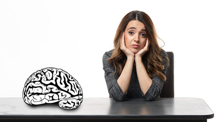 Young woman with a facial expression of boredom, sitting at her desk with face on her palms,...