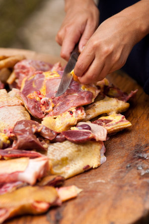 Young woman slicing raw chicken meat on a wooden table, a normal view in Romanian countryside