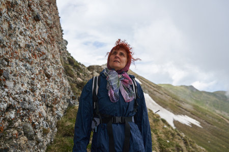 Woman hiker in raincoat with backpack hiking on a trail in the rocky mountains in a rainy day