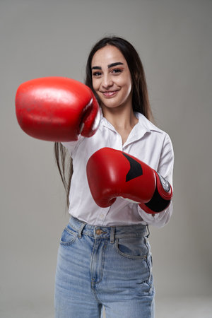 Young competitive businesswoman with red boxing gloves, conceptual image of fighting spirit, isolated on gray backgroundの写真素材