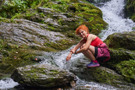 Woman hiker by a river with a waterfall in the mountains in the late summerの写真素材
