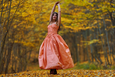 Autumn full length candid portrait of a beautiful woman in pink dress in the beech forest on a carpet of fallen leavesの写真素材