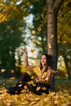 Hispanic beautiful young woman in a park surrounded by colorful trees and fallen leaves in a warm autumn dayの写真素材