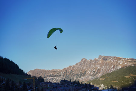 Person paragliding above a resort town in the Swiss Alps mountains, Switzerland