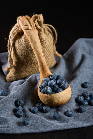 Hand sculpted wooden ladle filled with fresh blueberries on a gray kitchen clothの写真素材