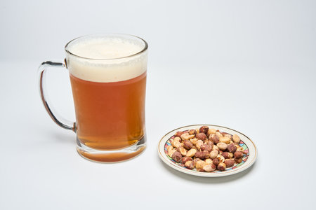 A glass mug with blonde beer and a plate with salted peanuts isolated on white backgroundの写真素材
