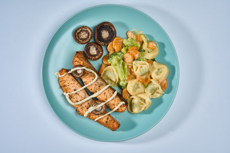 Airfryer grilled salmon fillets with tortellini garnish with spinach, carrots and broccoli and fried mushroomsの写真素材