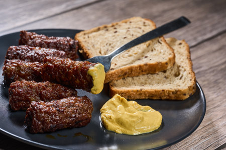 Grilled lamb and beef meat rolls with mustard and bread on a wooden boardの写真素材