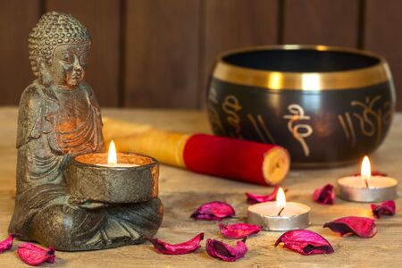 stone sitting buddha, candles and Tibetan bowl. Around the candle, the atmosphere for meditation. Home comfort and relaxationの写真素材