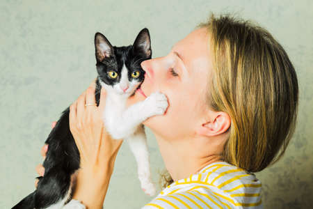 Life style photo of a casual dressed female who is holding and petting and kissing cute a cat. cat...