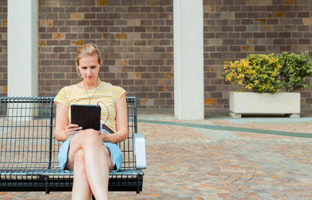 A young beautiful girl using tablet while sitting on the park bench.