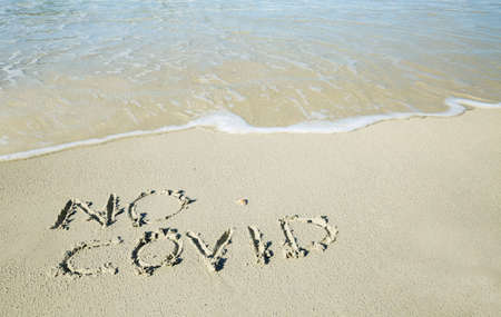 No covid written on the sand of the shore of a beach with incoming waves. Fear of beach resort...