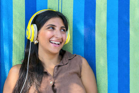 Smiling attractive young woman in headphones standing and listening to music over colorful background.の写真素材