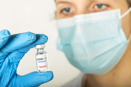 Doctor with blue gloves is holding a vial of vaccine or drug on a white background. Vaccination...