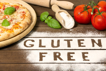 A gluten free pizza on a rustic wood background, with word "gluten free" made of flour, tomato, basil, spoon of flour. close upの写真素材