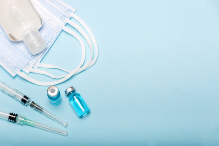 Medical bottle, hand sanitizer, vials, syringes and face mask on blue background with copy space. Vaccination session and immunity improvement.の写真素材
