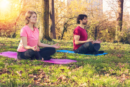 Yoga class. Joyful peaceful people sitting in the lotus pose while practicing yoga outdoorsの写真素材