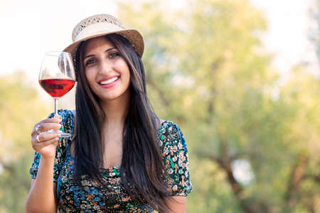Young happy woman with straw hat and glass of red wine, on backgroundの写真素材