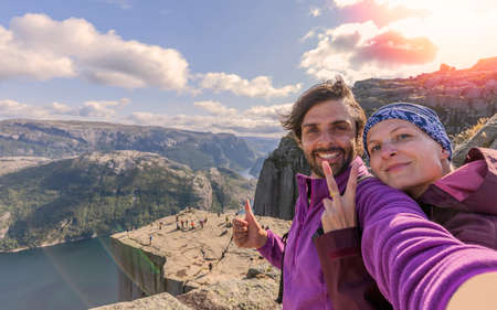 A cheerful couple in the summit of the Pulpit Rock (Preikestolen), one of the world's most spectacular viewing points. A plateau that rises 604 meters above the Lysefjord, Norwayの写真素材