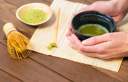 Girl's hands holding matcha tea in special traditional Japanese matcha tea bowl with bamboo spoon and whisk and matcha tea powderの写真素材