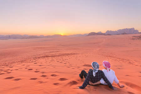 A young couple is watching at sunrise over wadi rum desert in Jordanの写真素材