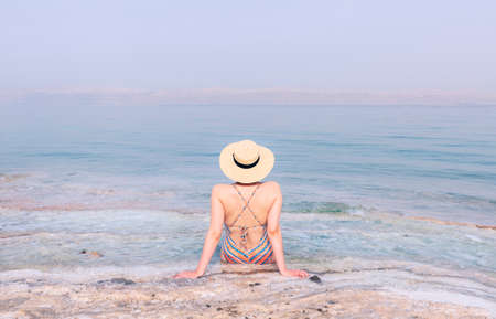 Attractive girl in swimsuit with hat sitting on the shore of the dead seaの写真素材