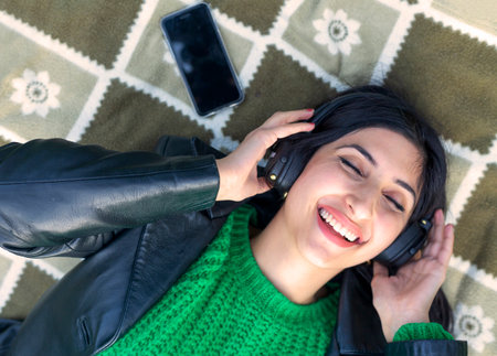 photo of young cheerful girl happy positive smile lying blanket listen music headphones outdoors