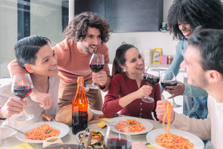 Multiethnic friends eating pasta and drinking wine at homeの写真素材