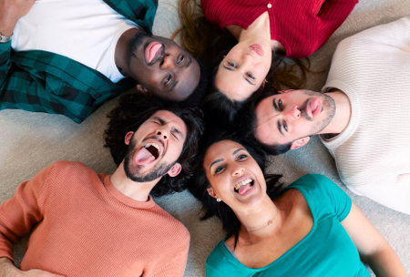 Diverse group of friends lying down taking silly selfies in circle, pulling face