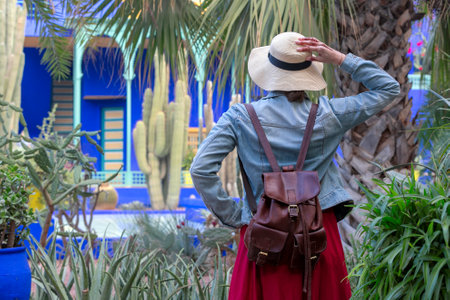 A young woman in a hat with and backpack is standing on a bamboo alley track with colorful pots and holding her hat in her hands. Jardin Majorelle. Marrakech, Moroccoの写真素材