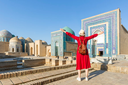 Young tourist dressed in red with arms raised in front of the Shah-I-Zinda memorial complex in...