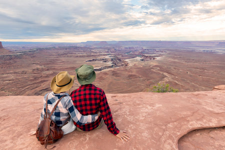 Couple with scenic view on Buck Canyon seen from Mesa Arch near Moab, Canyonlands National Park, San Juan County, Utah, USA. Looking at natural pothole arch rock formation near Island in the Sky Mesaの写真素材