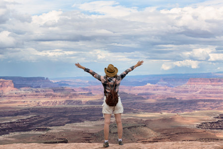 Adventurous woman on the edge of a cliff is looking at a beautiful landscape view in the Canyon during a vibrant sunset. Utah, United States.の写真素材