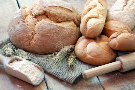 Close up of fresh bread, bowl of flour, wheat grains and spikelets on wooden table
