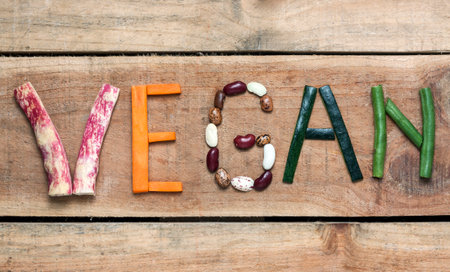 The word "Vegan" written with vegetables, fruits, nuts and legumes on rustic wooden background, concept - organic ingredients for healthy vegan food and lifestyleの写真素材