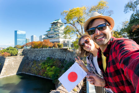 A young tourist couple taking a selfie with Japan flag at Osaka Castle, Osaka Castle is one of the...