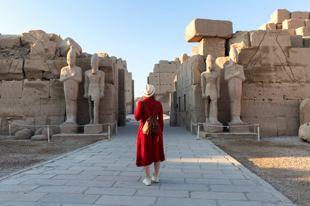 A visitor in a red dress explores the ancient colonnade at the Karnak Temple in Luxor.の写真素材