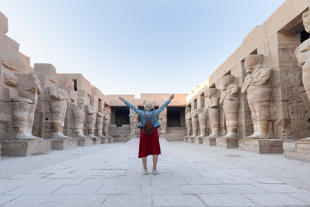 A happy tourist girl in a dress is interested in Egyptology and archeology and gets a travel experience at the Karnak Temple in Luxor.の写真素材