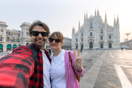 Happy couple taking selfie in front of Duomo cathedral in Milan, Lombardy - Two tourists having fun on summer vacation in Italyの写真素材