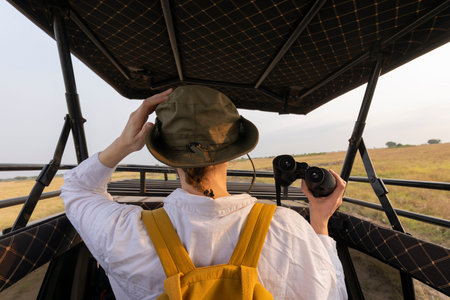 People sitting in specialized open safari vehicle, looks through binoculars and filmed on mobile phone. Travel in savannah, observe wild animals in natural habitat.の写真素材