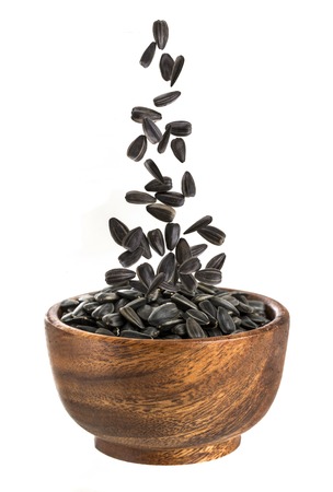 Sunflower seeds in wooden bowl. Falling sunflower seeds on a white backgroundの写真素材