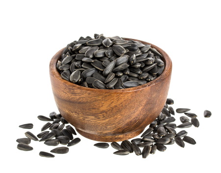 Black sunflower seeds in a wooden bowl, isolated on white background with clipping pathの写真素材