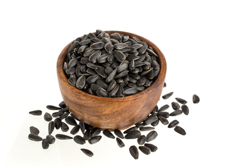 Black sunflower seeds in a wooden bowl, isolated on white backgroundの写真素材