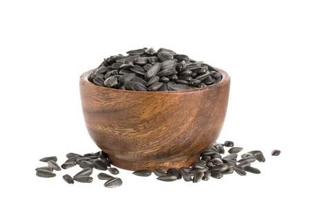 Black sunflower seeds in a wooden bowl, isolated on white background with clipping pathの写真素材