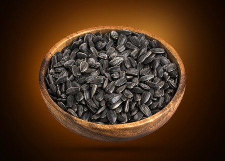 Black sunflower seeds in a wooden bowl, isolated on white background with clipping pathの写真素材