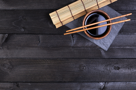 Background for sushi. Bamboo mat, soy sauce, chopsticks on dark table. Top view with copy spaceの写真素材