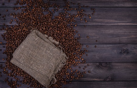 Coffee background, top view with copy space. Burlap bag and coffee beans on dark wooden backgroundの写真素材