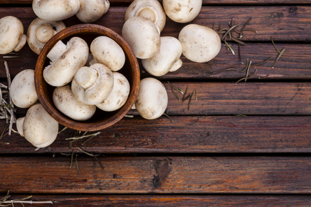 Fresh white mushrooms champignon in brown bowl on dark wooden background. Top view. Copy space.の写真素材
